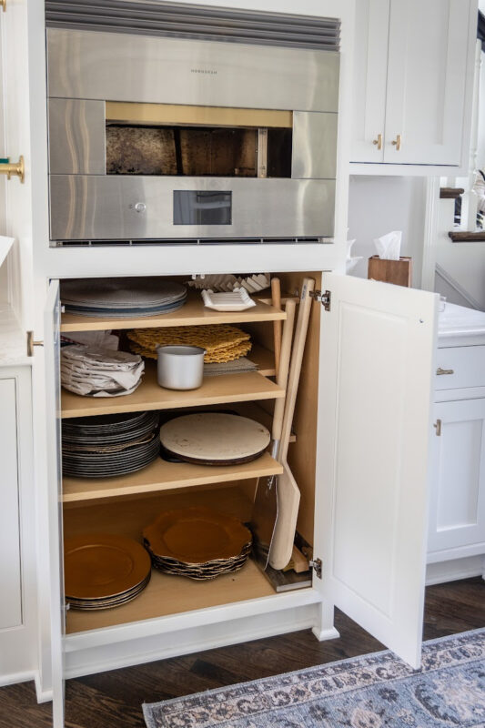 White painted kitchen cabinets with doors open showing shelves with baking dishes under an oven.