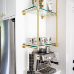 White painted coffee bar cabinets with gold shelf system above coffee maker.