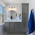 Bathroom with gray painted vanity cabinets and a circular mirror.