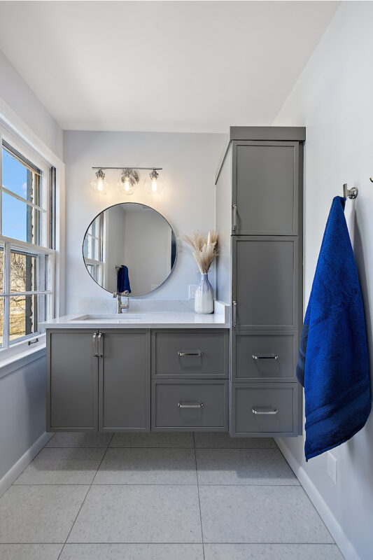 Bathroom with gray painted vanity cabinets and a circular mirror.