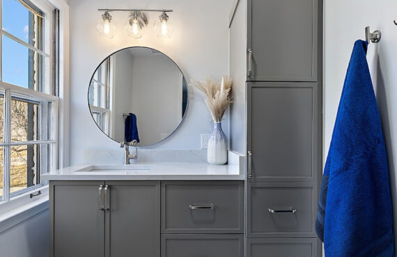 Bathroom with gray painted vanity cabinets and a circular mirror.