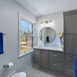 Bathroom with gray painted vanity cabinets and a circular mirror.