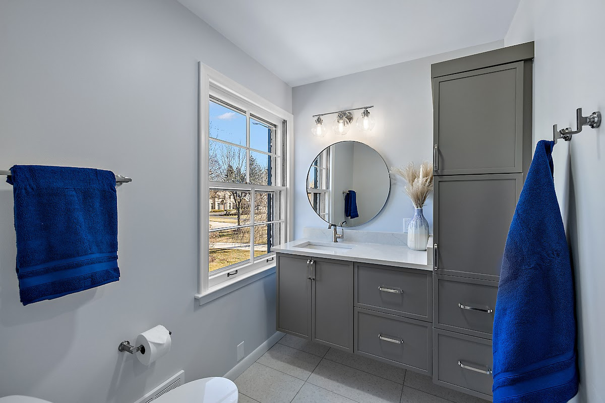 Bathroom with gray painted vanity cabinets and a circular mirror.
