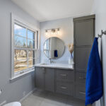 Bathroom with gray painted vanity cabinets and a circular mirror.