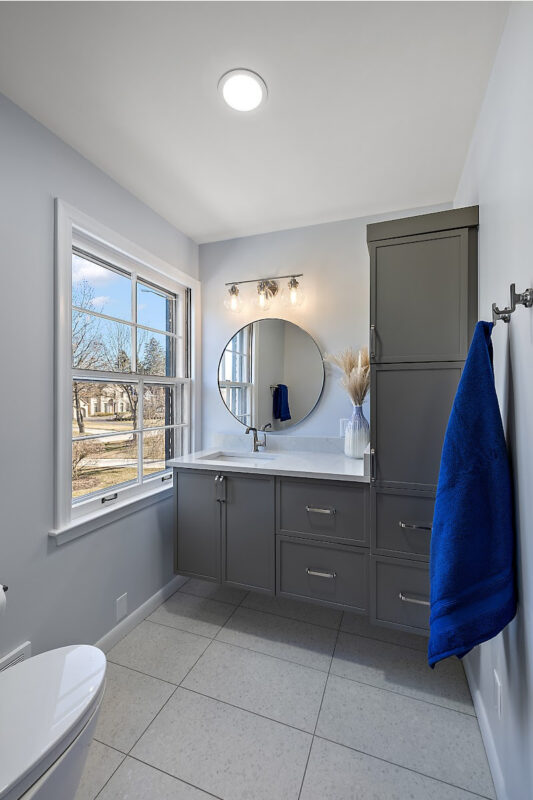 Bathroom with gray painted vanity cabinets and a circular mirror.