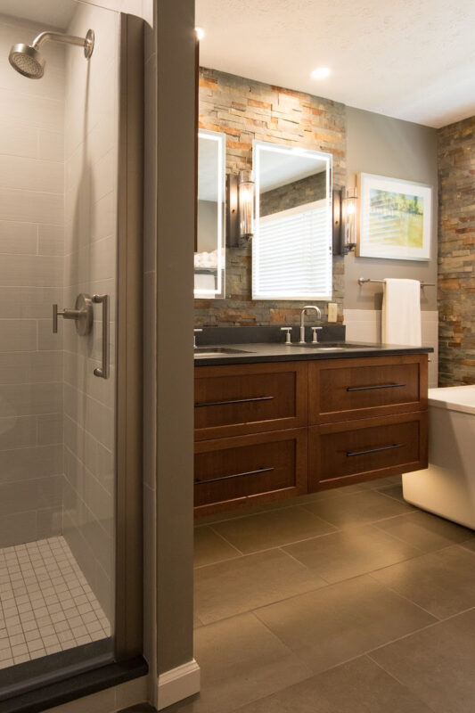 Floating vanity finished in Autumn stain near a large white tub.