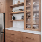 Light brown stained cabinets with floating shelves and glass doors on a countertop cabinet