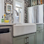 Painted green kitchen cabinets with unique wallpaper showing farm sink