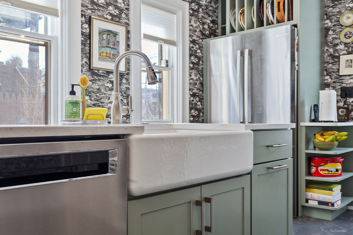 Painted green kitchen cabinets with unique wallpaper showing farm sink