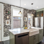 Painted green kitchen cabinets with unique wallpaper showing farm sink in the island