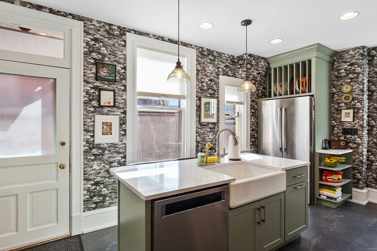 Painted green kitchen cabinets with unique wallpaper showing farm sink in the island