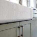 Painted green kitchen cabinets with unique wallpaper showing close up of farm sink