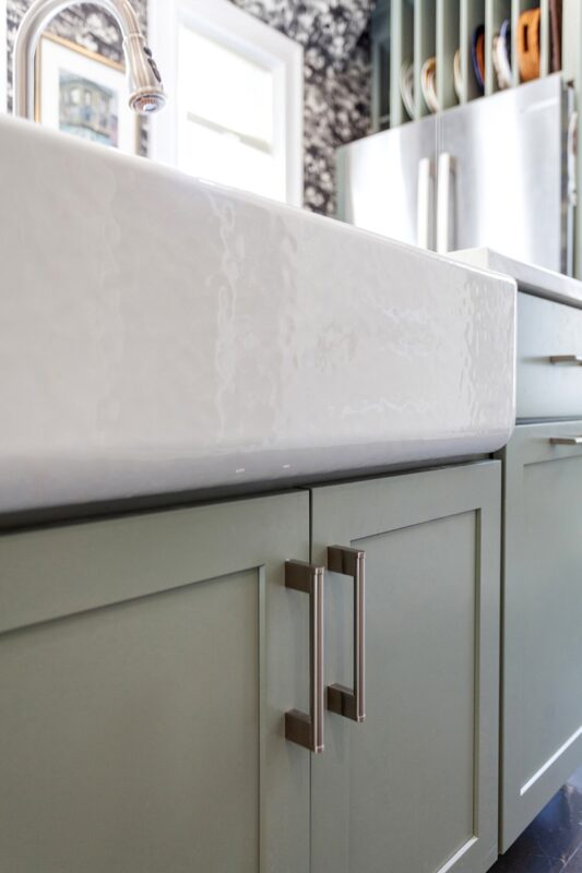 Painted green kitchen cabinets with unique wallpaper showing close up of farm sink