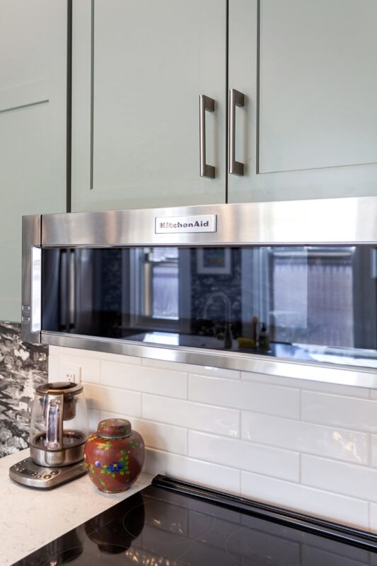 Painted green kitchen cabinets with unique wallpaper showing close up of microwave