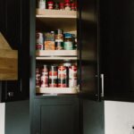 Black painted kitchen cabinets. Showing open door of a countertop cabinet with food items inside.