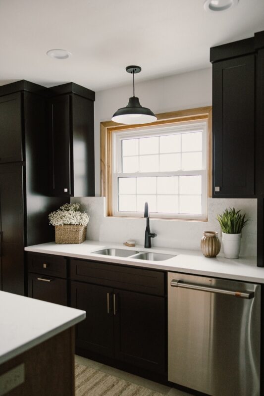 Black painted kitchen cabinets. View of kitchen sink with window above.