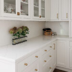 White kitchen with glass doors on two cabinets showing dishware.