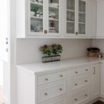 White kitchen with glass doors on two cabinets showing dishware.