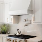 White kitchen. View of range below hood with a pot faucet.