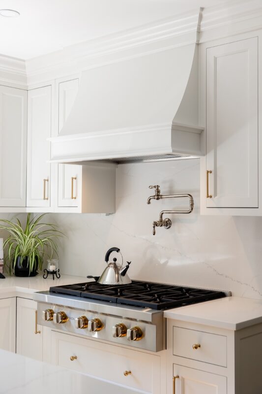White kitchen. View of range below hood with a pot faucet.
