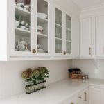 White kitchen with glass doors on two cabinets showing dishware.