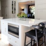 White kitchen island with black stool seating and in-cabinet microwave under counter.