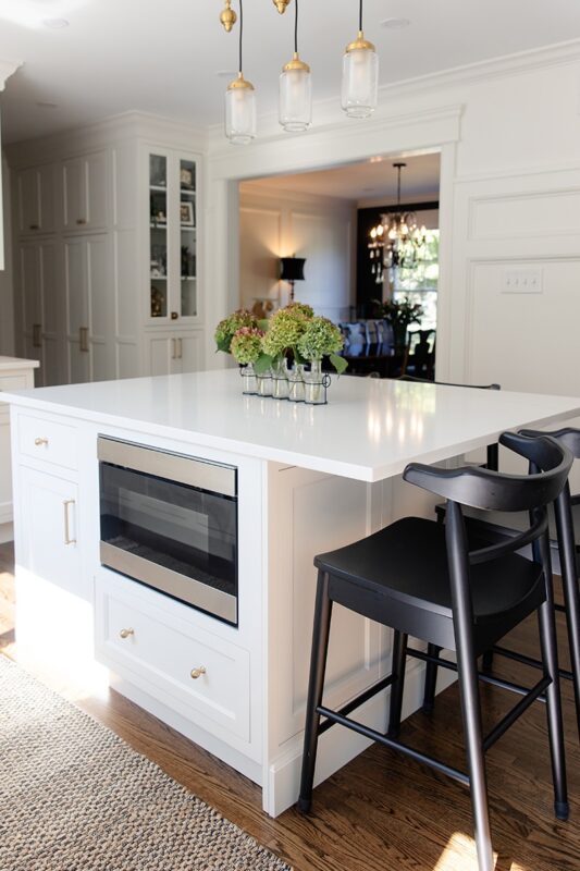 White kitchen island with black stool seating and in-cabinet microwave under counter.