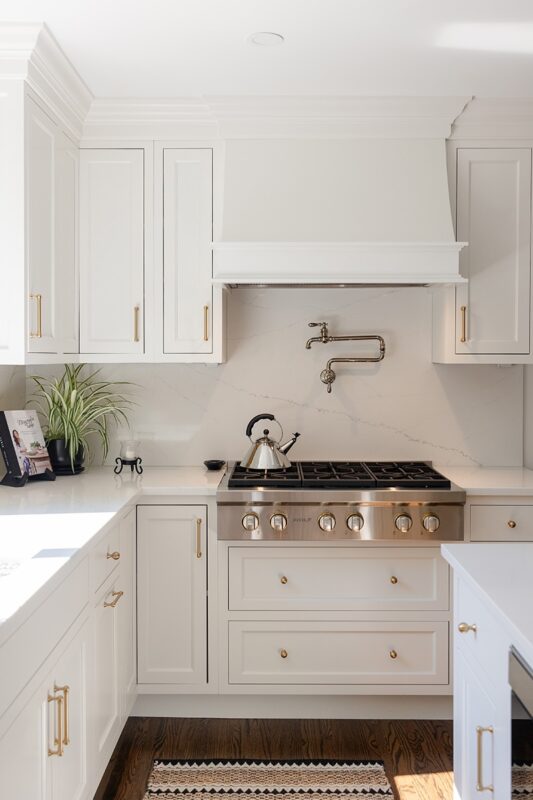 White kitchen. View of range below hood with a pot faucet.
