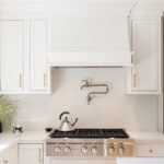 White kitchen. View of range below hood with a pot faucet.