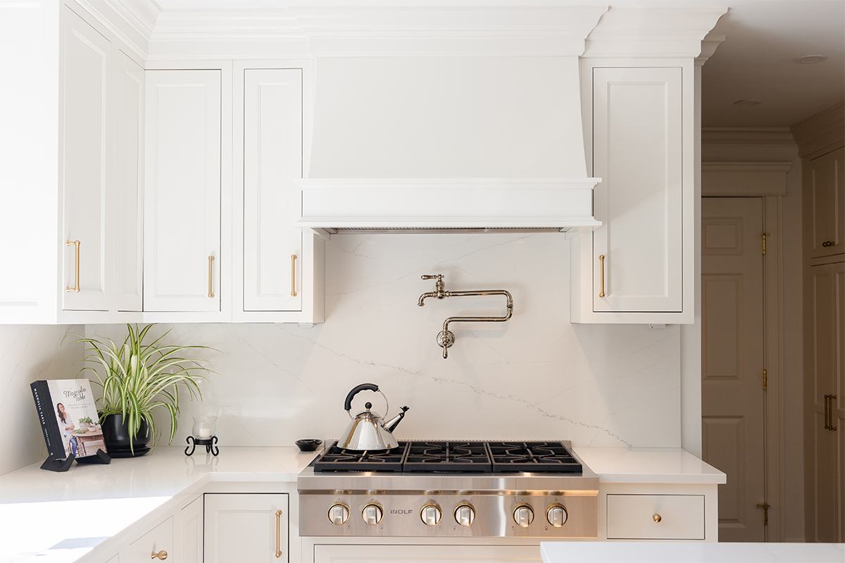 White kitchen. View of range below hood with a pot faucet.