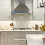 White painted kitchen cabinets and stainless steel blower above cooktop.