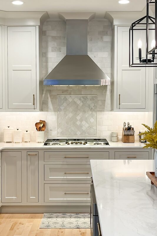 White painted kitchen cabinets and stainless steel blower above cooktop.
