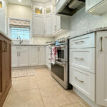 White painted kitchen perimeter cabinets and walnut natural island. View close to floor towards the window above a sink.
