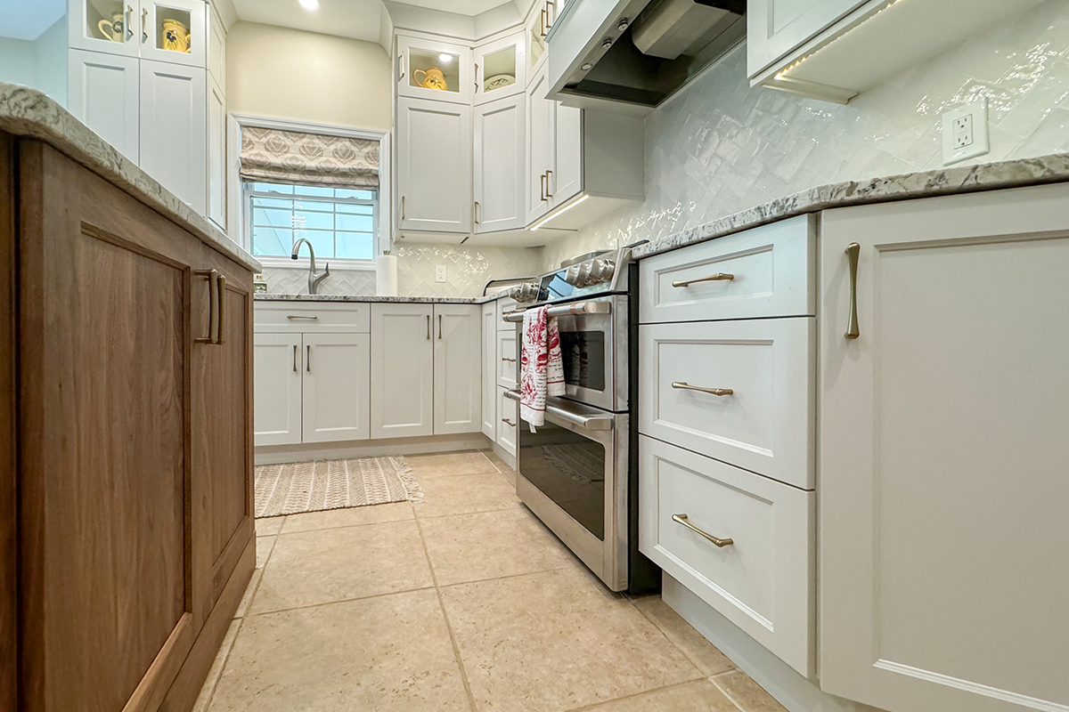 White painted kitchen perimeter cabinets and walnut natural island. View close to floor towards the window above a sink.