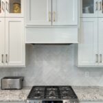 White painted kitchen perimeter cabinets. View of painted hood above a stove.