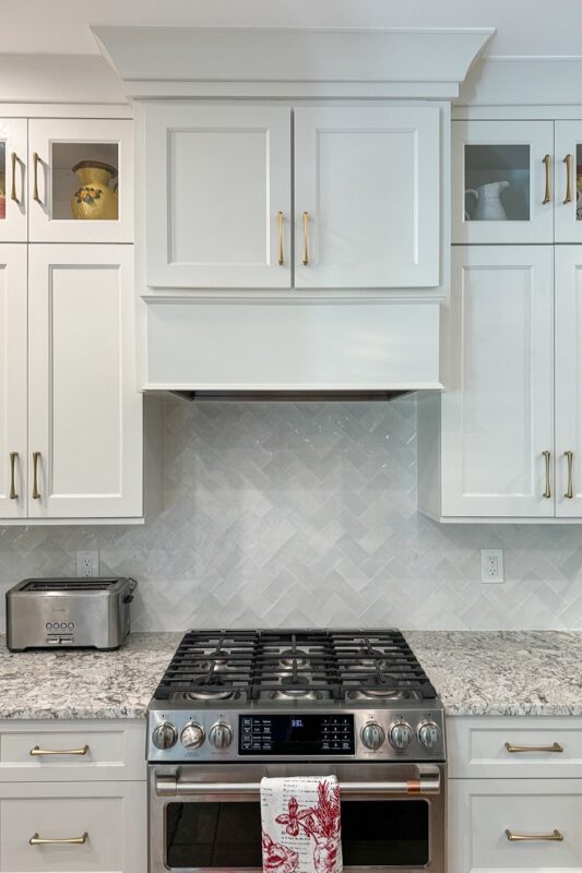 White painted kitchen perimeter cabinets. View of painted hood above a stove.