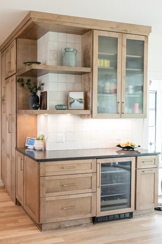 Stained kitchen cabinets with open shelves, glass door upper cabinet and beverage cooler below.
