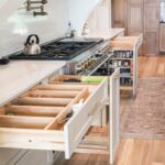 White painted kitchen cabinets with drawer open showing cutlery divider box and pull out accessories on each side of stove