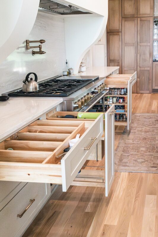White painted kitchen cabinets with drawer open showing cutlery divider box and pull out accessories on each side of stove