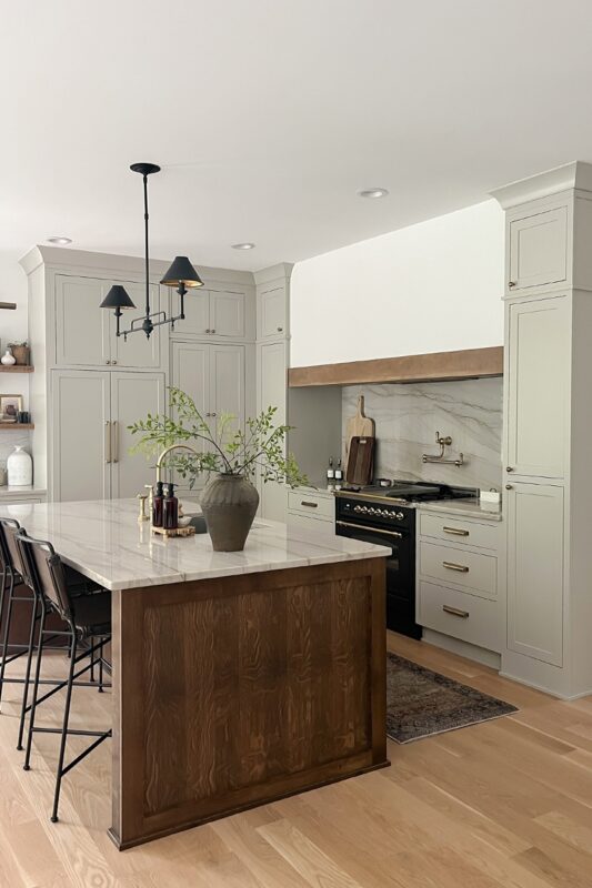 Small painted kitchen. Cabinets in light gray paint. Box hood painted white with stained brown accent that matches the stained island.
