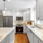 White-painted kitchen perimeter cabinets with a gray-painted island.