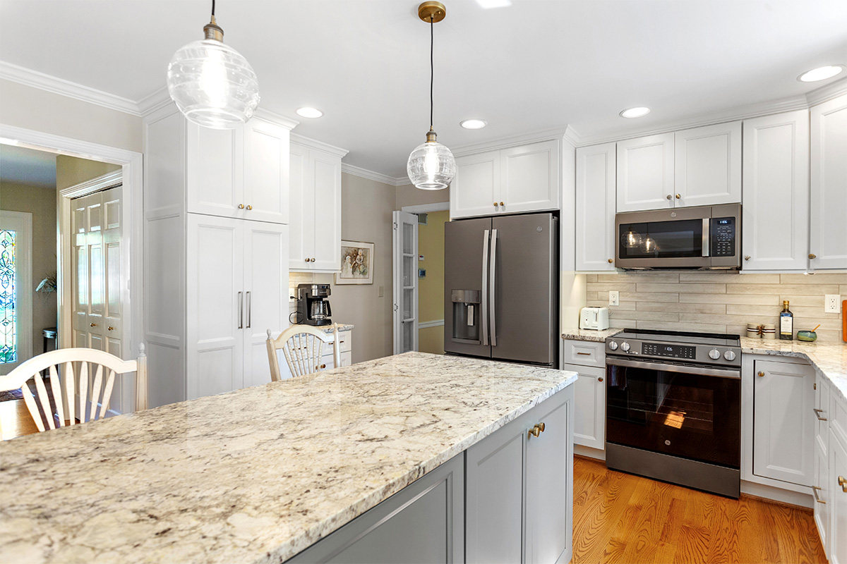 White-painted kitchen perimeter cabinets with a gray-painted island.