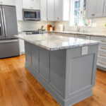 White-painted kitchen perimeter cabinets with a gray-painted island.
