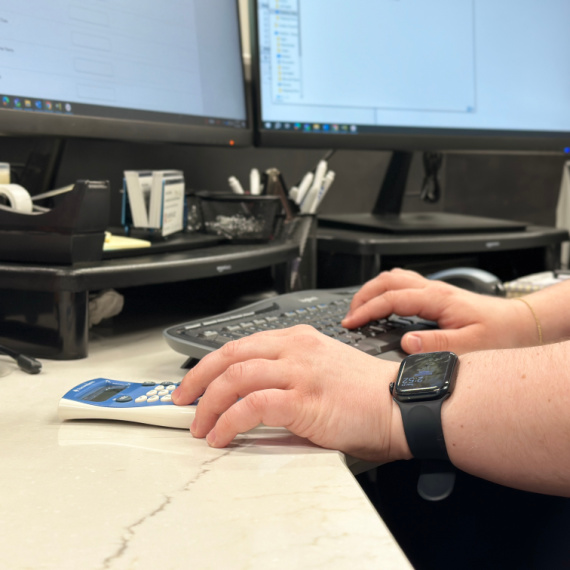 Hands working on a computer and using a calculator