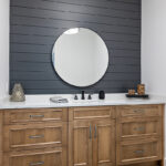 Powder bathroom with brown stained vanity cabinet and a round mirror on a shiplap blue painted wall.