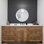Powder bathroom with brown stained vanity cabinet and a round mirror on a shiplap blue painted wall.