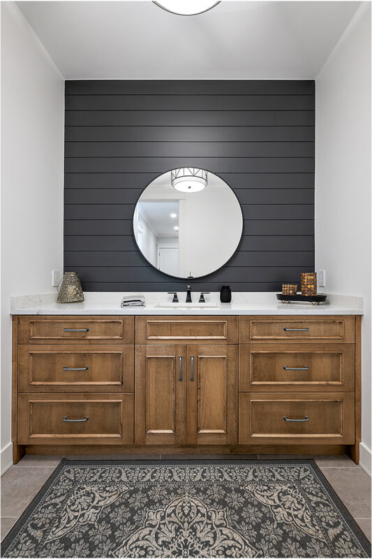 Powder bathroom with brown stained vanity cabinet and a round mirror on a shiplap blue painted wall.
