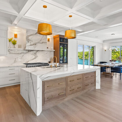 White kitchen cabinets with brown stained island with marble waterfall counter and hood