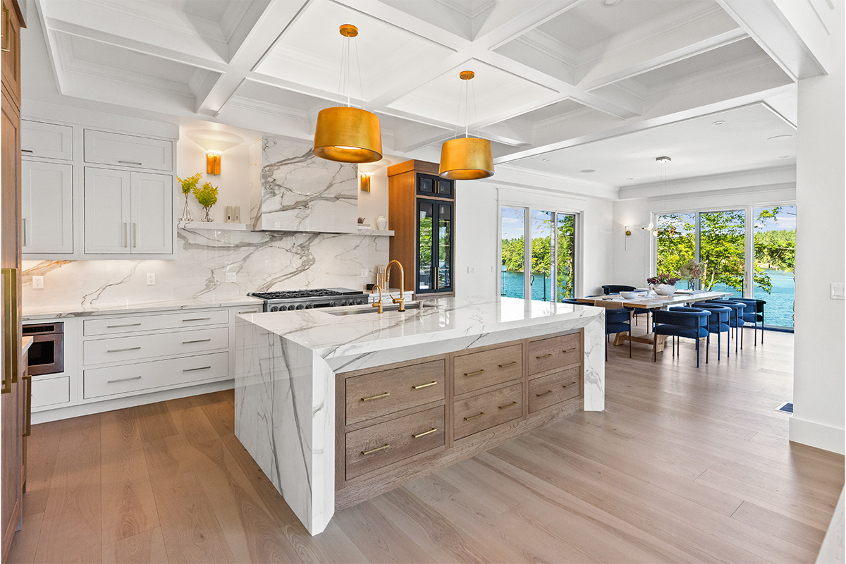 White kitchen cabinets with brown stained island with marble waterfall counter and hood