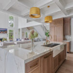 White kitchen cabinets with brown stained island with marble waterfall counter and hood